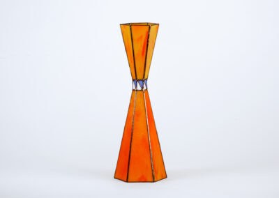 A tall orange stained glass vase with a narrow middle and blue accents.