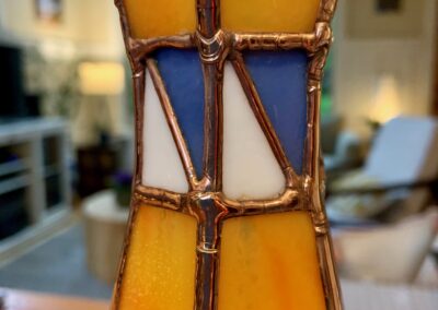 A stained glass artwork featuring a sailboat design with yellow and blue colors.
