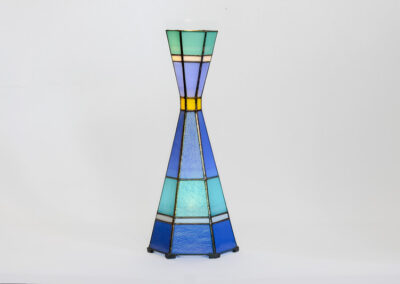 A tall, hourglass-shaped stained glass lamp with blue and green panels.