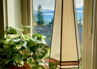 A tall beige lamp next to a green leafy plant by a window.