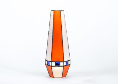 A tall, tapered vase with geometric color blocks in orange, white, and blue.