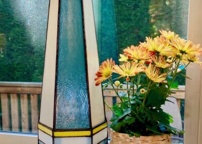 A modern geometric vase with a blue flower on a table beside a basket of yellow flowers.
