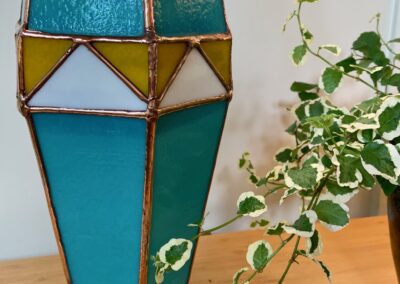 A stained glass lantern with blue and yellow panels beside a green vine plant.