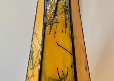 A tall, yellow stained glass vase with black abstract lines.